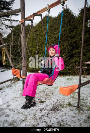 Happy little girl swinging on playground at snowy winter day Stock Photo