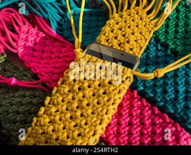 Small bags knitted using the macrame technique from cotton cord. Multi-colored bags for mobile phones on a wooden background. Stock Photo