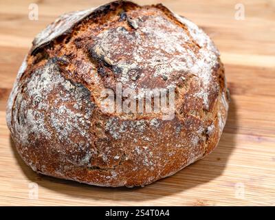 A close-up image of a rustic, round homemade bread resting on a wooden surface. Stock Photo