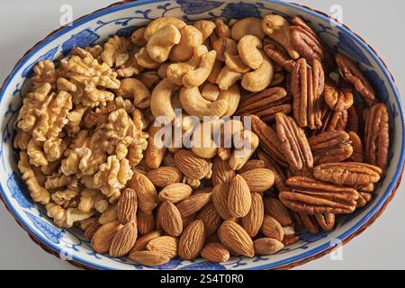 Assorted nuts in a stoneware container with a straw basket, on a white background. Almonds, Walnuts, Cashews and Chestnuts Stock Photo