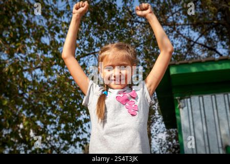 Portrait of happy little girl holding hands up at park at sunny day Stock Photo