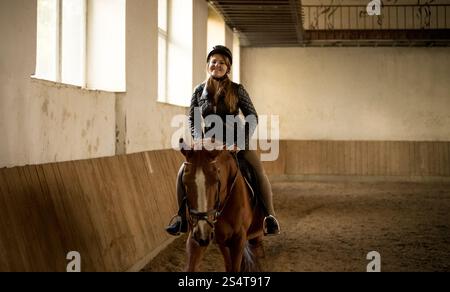 Portrait of woman riding beautiful brown horse at indoor manege Stock Photo