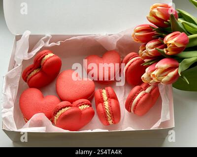 French dessert red hearts macarons in the white box and red tulips on the white background Stock Photo