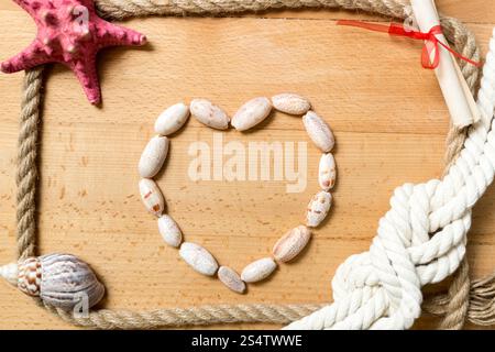 Heart made of seashells with border of ropes and knots on wooden background Stock Photo