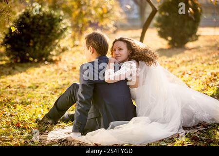 Portrait of beautiful happy bride hugging groom sitting on yellow leaves at park Stock Photo