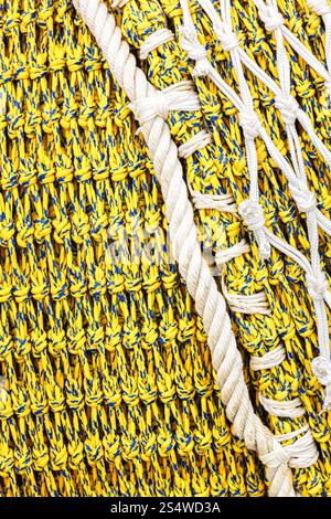 Close-up view of a traditional fishing net made of yellow and blue cords intertwined with white ropes. Stock Photo