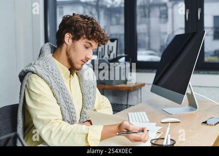 Curly-haired young man in smart casual attire focuses on his tasks at a modern workspace. Stock Photo