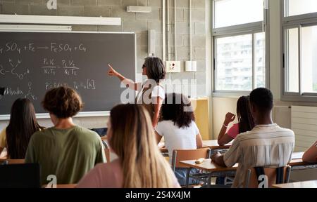 Teacher Explaining Chemistry Formulas to Students in a Classroom Setting. Stock Photo