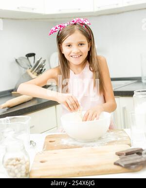 Beautiful little girl with pink bow on hair making dough in big bowl Stock Photo