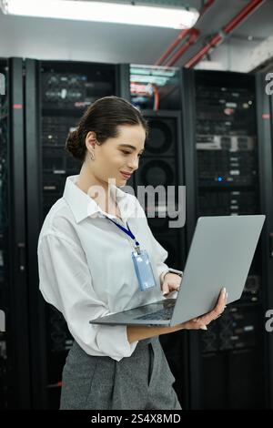 IT specialist in a white shirt engages with a laptop among server hardware in a data center. Stock Photo