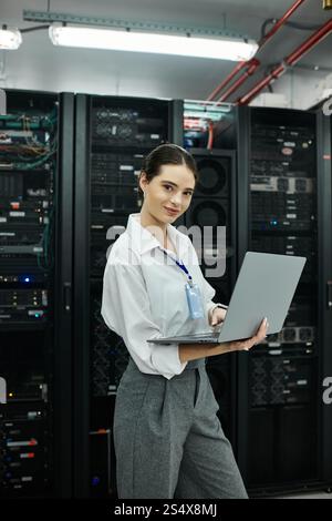 Woman in a white shirt is efficiently working on a laptop in a sophisticated server room. Stock Photo