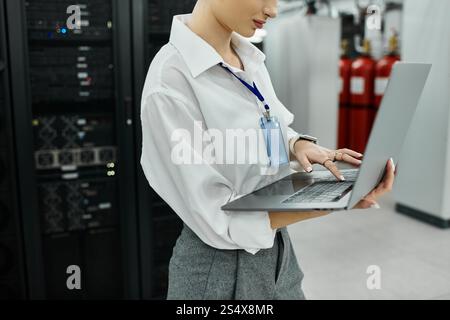 Dedicated IT expert in a white shirt works with laptop amidst advanced server hardware. Stock Photo