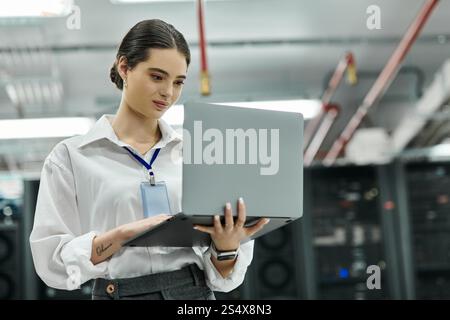 IT specialist reviews data on her laptop in a high-tech server room environment. Stock Photo