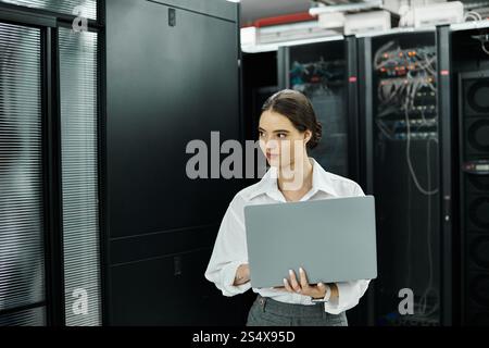 A professional woman in a white shirt works on her laptop in the server room for security. Stock Photo