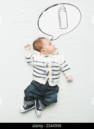 Cute little boy lying on bed and dreaming of bottle with milk Stock Photo