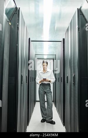A woman in a white shirt uses her smartphone while managing server operations in IT. Stock Photo