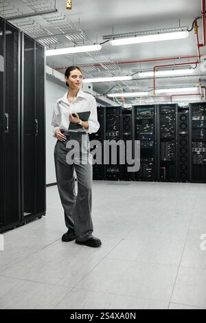 A professional woman in a white shirt stands confidently in a high-tech server room. Stock Photo