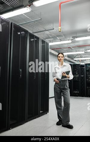 A skilled woman in a white shirt checks systems while managing server hardware in a tech hub. Stock Photo