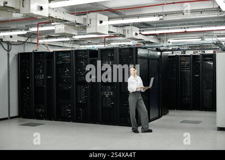 In a modern server room, a woman in a white shirt manages computer systems with focus and skill. Stock Photo