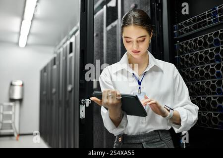 A woman in a white shirt supervises server operations using a tablet in a data center. Stock Photo