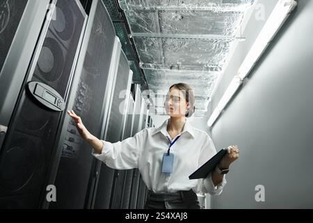 A woman in a white shirt manages server hardware in a contemporary data center setting. Stock Photo