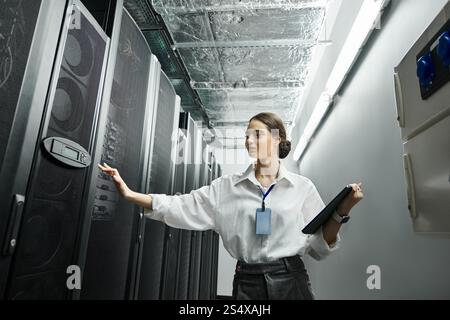 Woman in a white shirt engages with server hardware while maintaining digital security protocols. Stock Photo