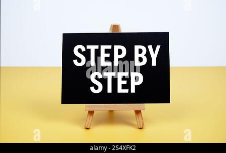 Step by step text written on paper card with easel standing on yellow background Stock Photo