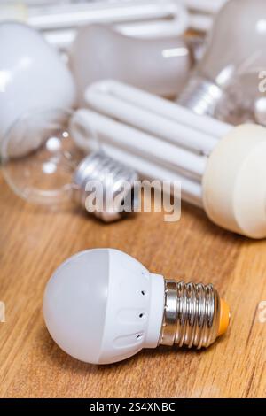 new LED lamp and pile of old incandescent light bulbs and used compact Fluorescent lamps on wooden board Stock Photo