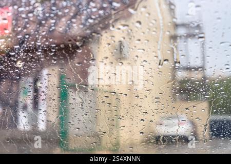 driving car in rain - rain trickles on windscreen and blurred house on background Stock Photo