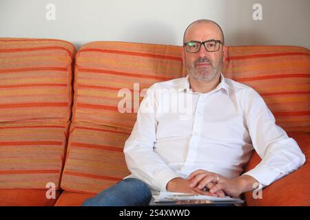 A calm, relaxed environment features a professional man on a couch with a clipboard, engaging in a focused, comfortable discussion Stock Photo