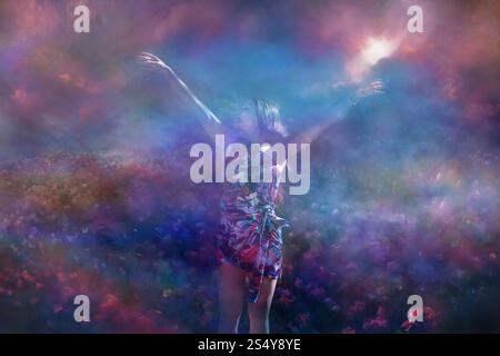 Young charming woman in an artistic dress, is standing with open feeling arms, in front of a wide Tulip field at a rising morning sun of spring, behin Stock Photo