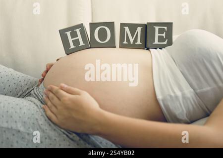 Closeup image of pregnant woman holding word Home on belly Stock Photo