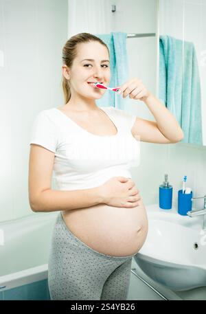 Portrait of beautiful pregnant woman brushing teeth in bathroom at morning Stock Photo