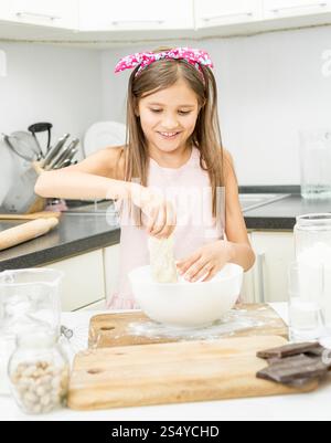 Beautiful little girl with pink bow on hair making dough on kitchen Stock Photo