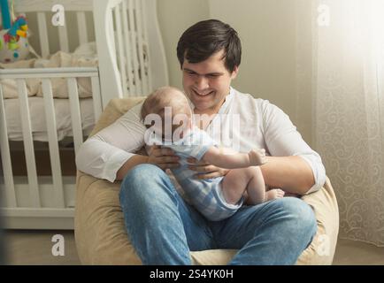 Young father sitting in bean bag chair and holding his little baby son Stock Photo