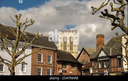 York Minster’s Central Tower, framed between Browns Department Store and The Roman Bath Pub, seen from St Sampson’s Square. York. Stock Photo