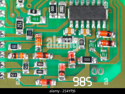 Closeup of surface mount assembly of electronic components on printed circuit board. Red or orange Zener diodes, black micro chip and small resistors. Stock Photo