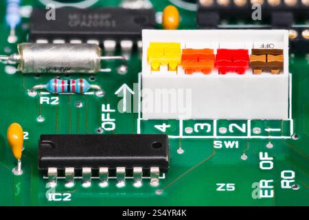 Closeup of various electronic components on printed wiring board. Colored 4 bit on-off DIP switch white package, black integrated circuit on green PCB Stock Photo