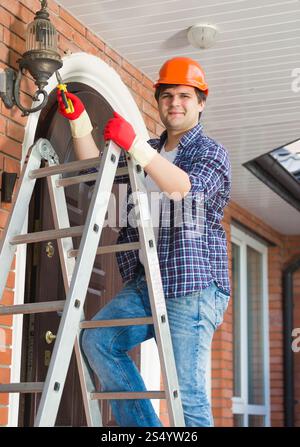 Electrician standing on stepladder and repairing outdoor lamp Stock Photo