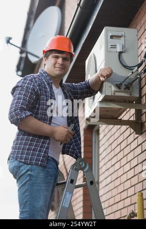 Young repairman installing air conditioner on outer wall Stock Photo