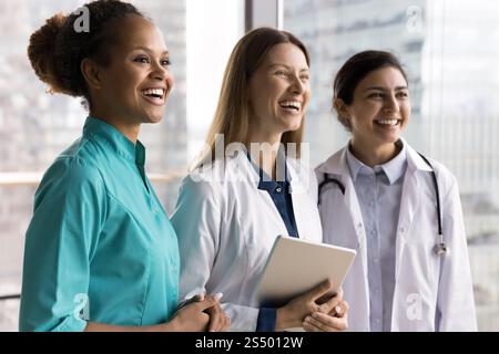 Three women GP standing in row, laughing, looking into distance Stock Photo