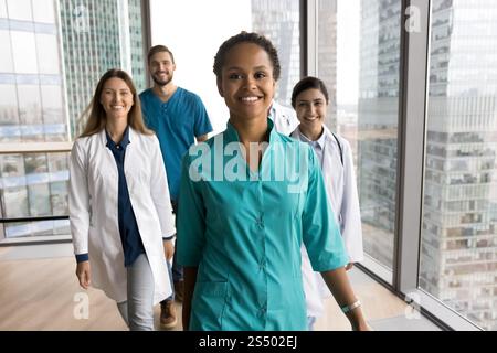 Doctors walking across clinic hallway led by African female colleague Stock Photo