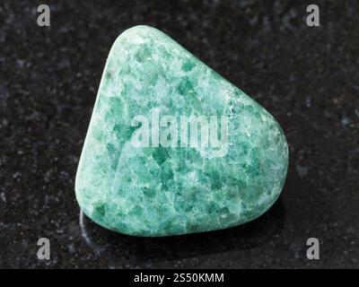 macro shooting of natural mineral rock specimen - tumbled green Jadeite gemstone on dark granite background Stock Photo