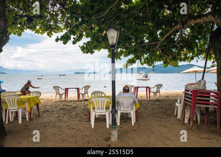 A man sits on Pontal Beach looking out to sea, Paraty, Rio De Janeiro State. Stock Photo