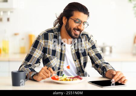 Happy indian guy having lunch and using digital tablet Stock Photo