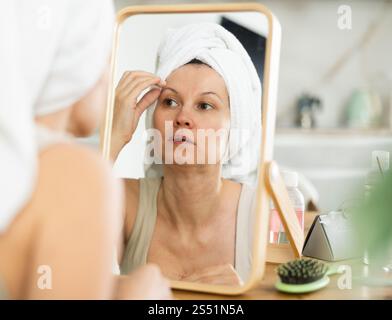 Middle-aged woman examining her facial skin looking in the mirror put on the table Stock Photo