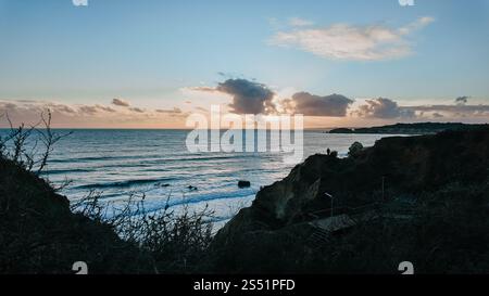 Looking out from the cliffs to the sunset in Portimão, Portugal, with the sun shining from behind clouds Stock Photo