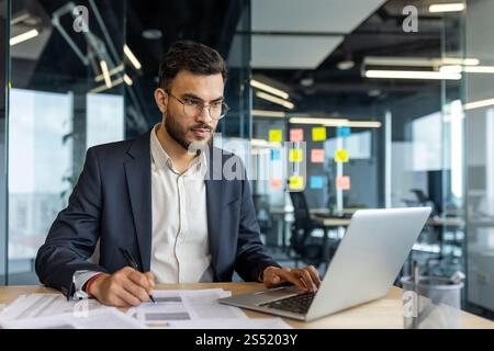 Serious thinking businessman doing paperwork inside office, man filling out paper tax forms, and signing documents and contracts. Successful financier investor preparing report. Stock Photo