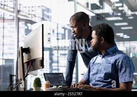 Data engineering IT staff members at PC desk developing machine learning algorithms. African american team in office solving tasks, training large scale deep learning models using computer Stock Photo
