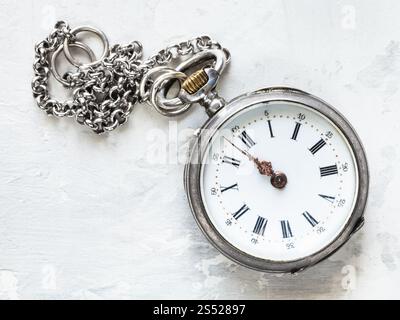 two minutes to twelve oclock on old pocket watch with chain on white concrete background Stock Photo